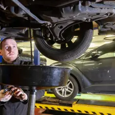 Mechanik spuszcza zużyty olej z samochodu, przygotowując się do wymiany oleju z filtrami.