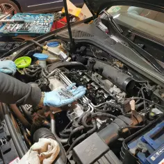 Mechanik wymienia wiązkę świec żarowych 1.9 TDI. Widać narzędzia i nowe świece w dłoniach.