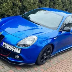 Niebieskie Alfa Romeo Giulietta z agresywnym bodykitem, czarnymi felgami i czerwonymi akcentami na zderzaku.