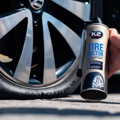 Puszka preparatu K2 Tire Doctor obok koła samochodowego.