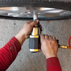 Mechanik w czerwonej bluzie używa klucza pneumatycznego do odkręcania śrub koła. Szybka wymiana opon to klucz do sprawnego sezonu.