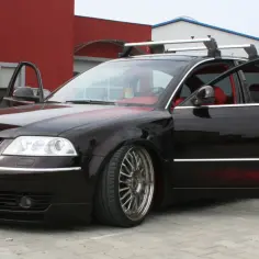 Czarny Passat B5 z body kitem i czerwonymi wstawkami, otwarte drzwi, czerwone wnętrze, relingi dachowe.