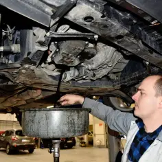 Mechanik spuszcza olej z silnika samochodu do miski.