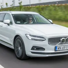 Białe Volvo V90 Cross Country w ruchu. Kierowca w okularach przeciwsłonecznych. Wiele pozytywnych volvo v90 cross country opinie potwierdza jego wszechstronność.