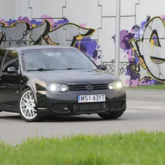 Czarny Golf 4 z tuningowym body kitem i białymi felgami, zaparkowany na tle kolorowego graffiti.
