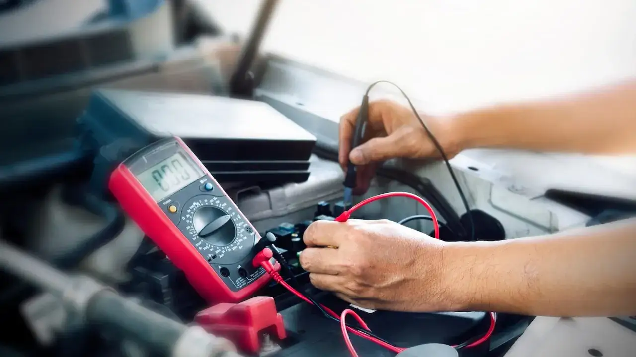 Mechanik sprawdza, czy alternator ładuje akumulator na postoju, używając multimetru.