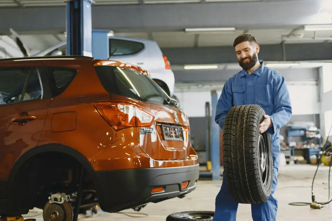 Mechanik z uśmiechem niesie nowe opony. Zastanawiasz się, ile zajmuje wymiana opon? To szybki proces!