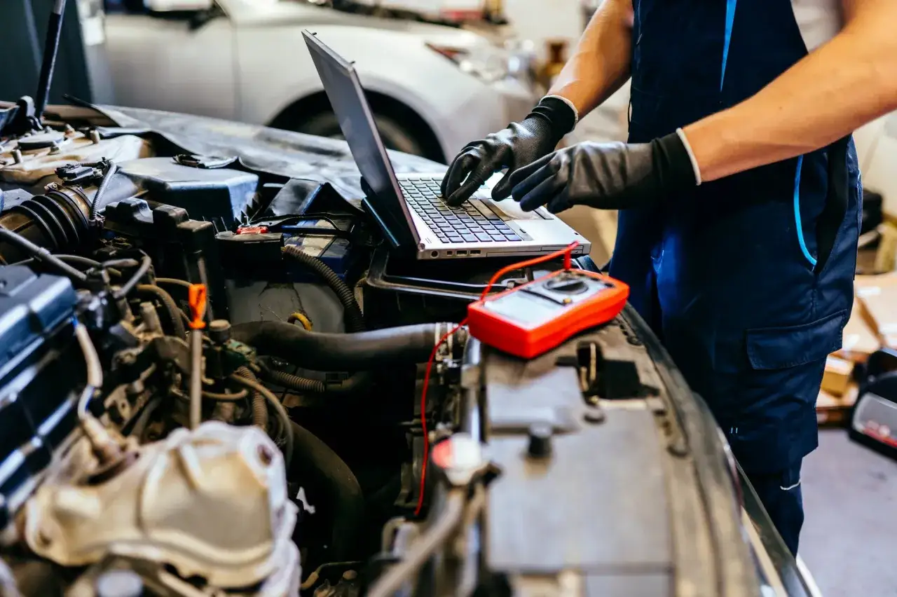 Mechanik diagnozuje klekotanie silnika benzynowego za pomocą laptopa i multimetru.