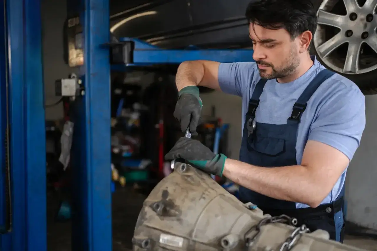 Mechanik naprawia uszkodzoną skrzynię biegów. Objawy awarii mogą być różne, ale ten mechanik wie, jak sobie z nimi poradzić.