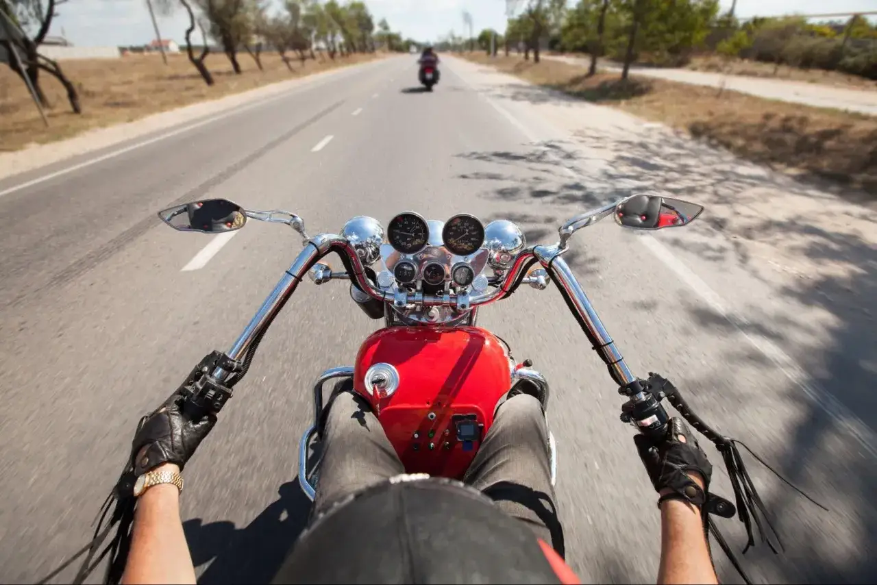 Widok z perspektywy kierowcy na kierownicę i deskę rozdzielczą czerwonego motocykla. W oddali inny motocykl. Nauka jak hamować motocyklem.