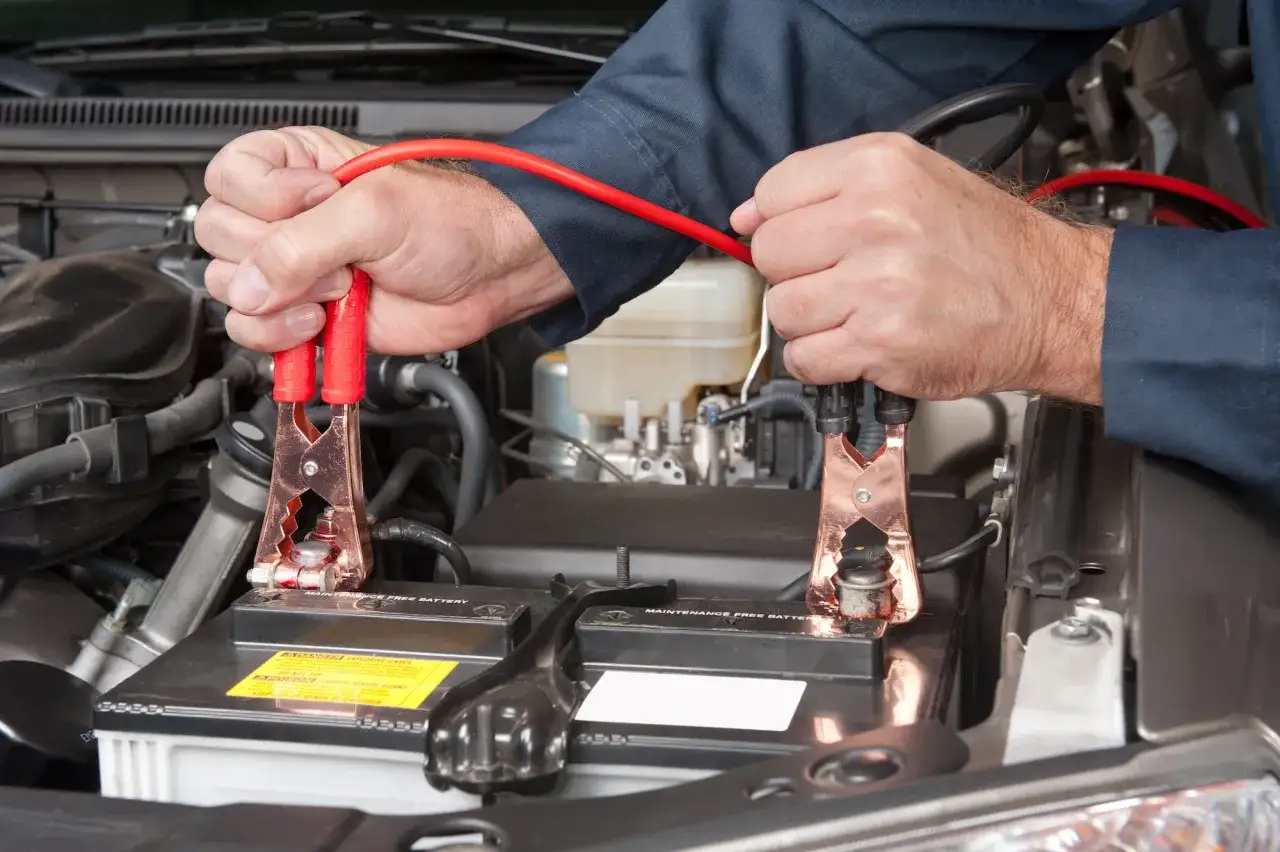 Ręce mechanika podpinają kable rozruchowe do akumulatora samochodowego, by uruchomić auto.