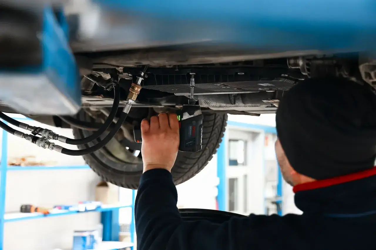 Mechanik używa wkrętarki do skrzyni biegów, pokazując, gdzie wlać olej do skrzyni biegów.