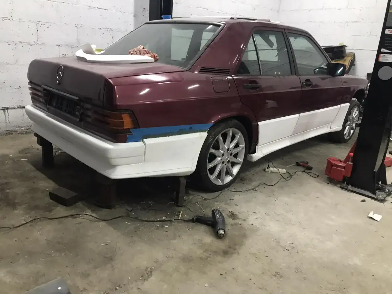 Mercedes 190 Evo z nowym body kitem w trakcie montażu. Karoseria w kolorze bordowym, elementy body kitu białe.