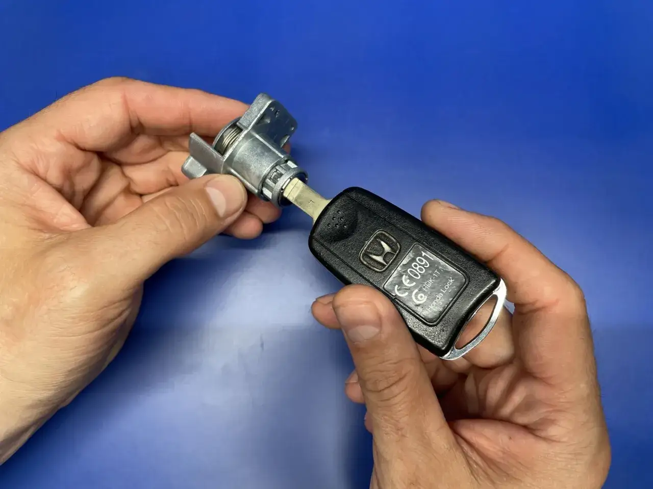 Dwie dłonie trzymają kluczyk samochodowy Honda i mechanizm zamka. Zastanawiasz się, ile kosztuje wymiana zamka w aucie?