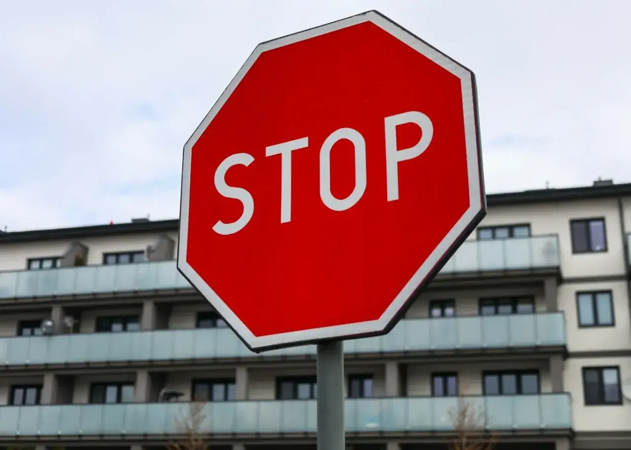 Czerwony znak STOP informuje kierowców, gdzie się zatrzymać. W tle nowoczesny budynek mieszkalny.
